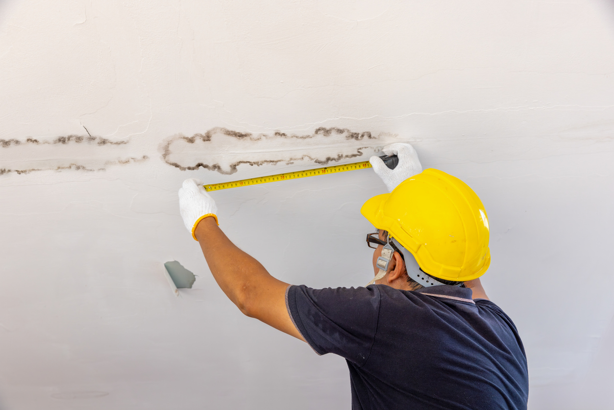 handyman measuring water leak damage on ceiling